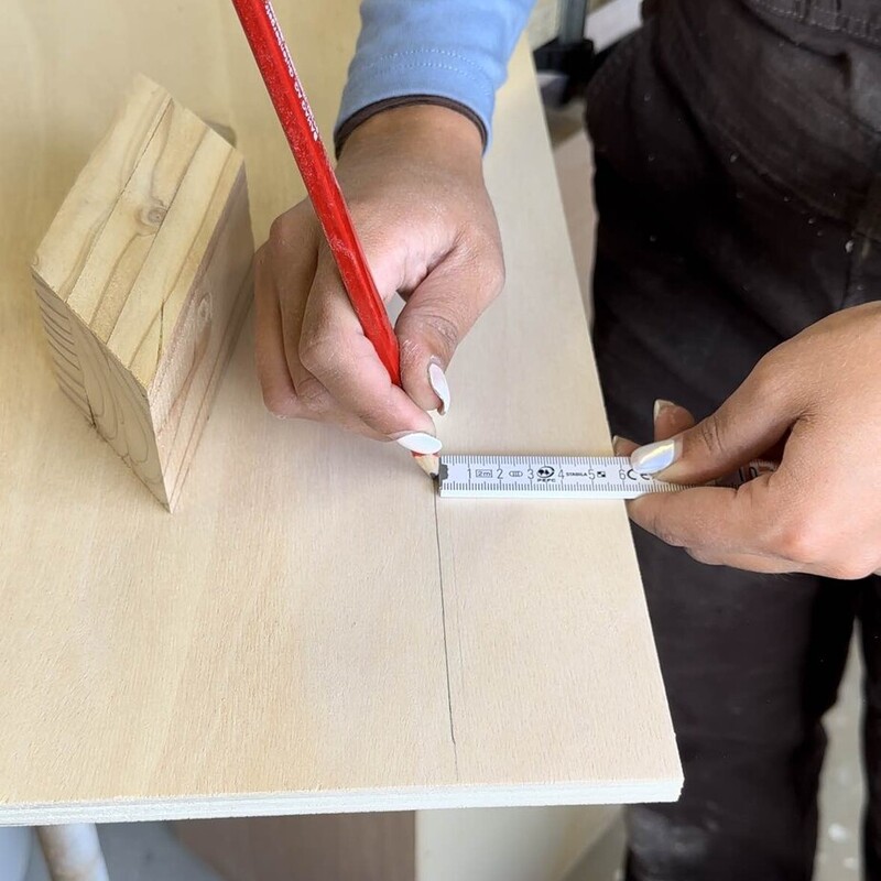 Frau zeichnet mit Bleistift und Meterstab Markierung auf Holz