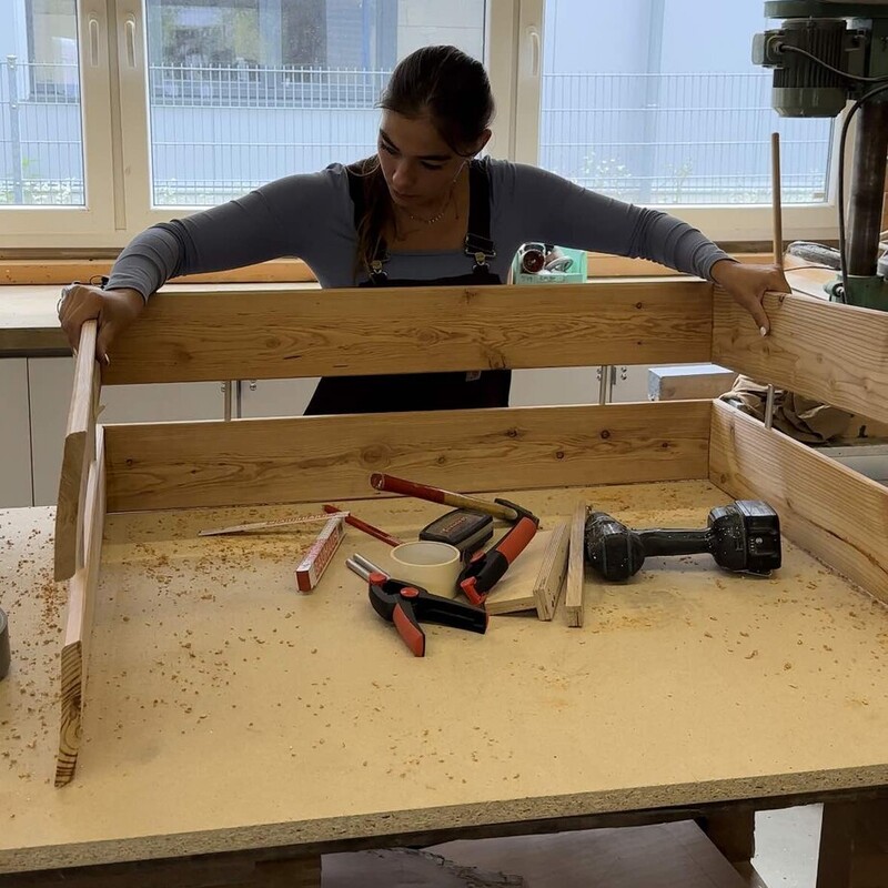 Frau steht in Werkstatt und baut Hundebett aus Holz