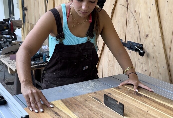 Frau mit Gehörschutz zersägt Holzplatte an Tischsäge