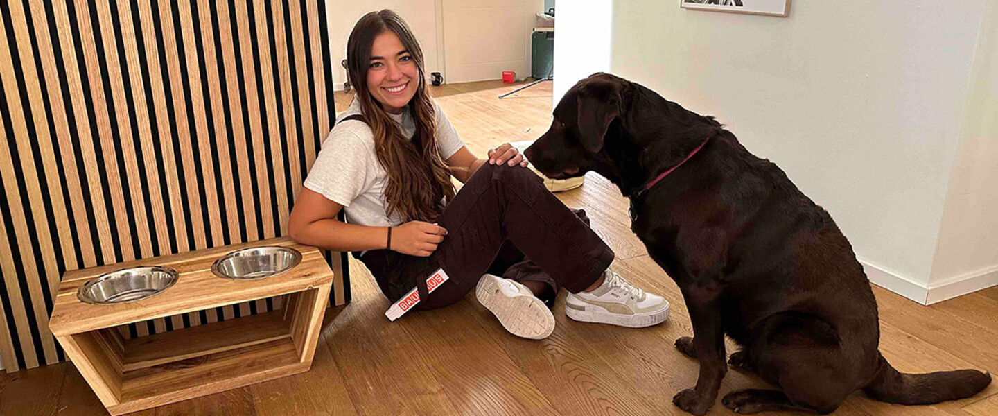Sitzende Frau und sitzender Hund neben Hundefressnapf