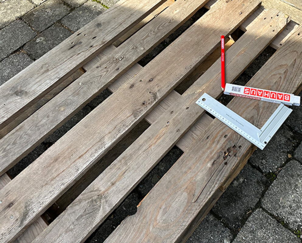 Meterstab, Bleistift und Schreinerwinkel liegen auf Europalette