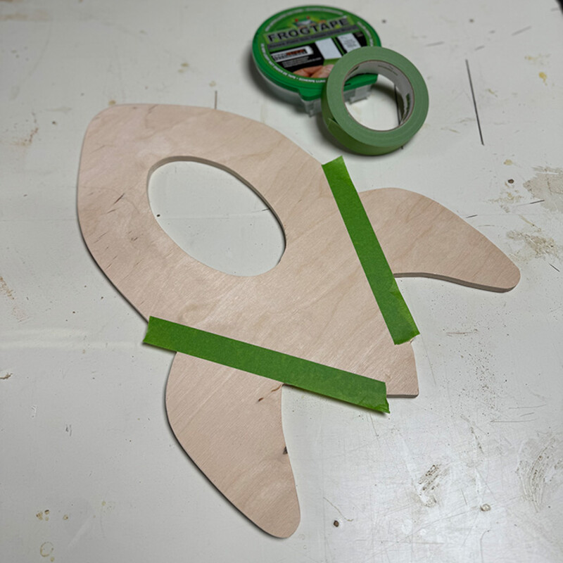 Mit grünem Klebeband beklebte Holz-Rakete liegt auf Werktisch