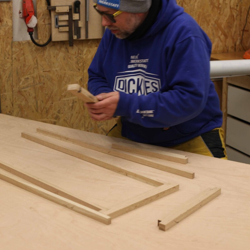 Robert Sike h&auml;lt in einer Werkstatt Holzst&uuml;cke in der Hand