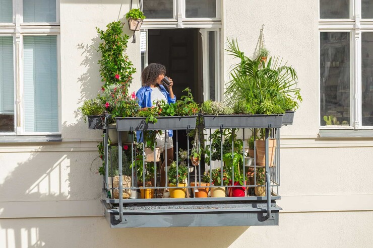 Eine Frau trinkt Kaffee auf ihrem bepflanzten Balkon.