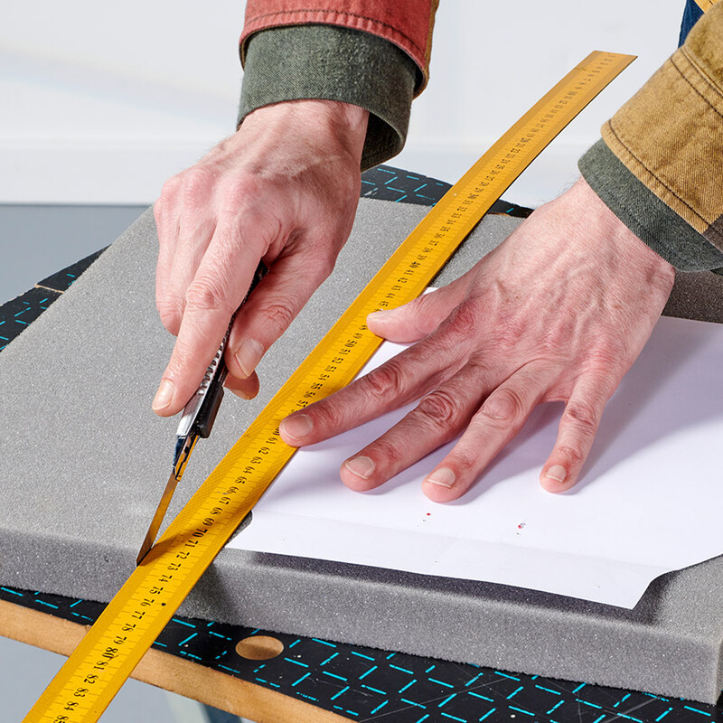 Mann schneidet Kunststoff mit Cuttermesser