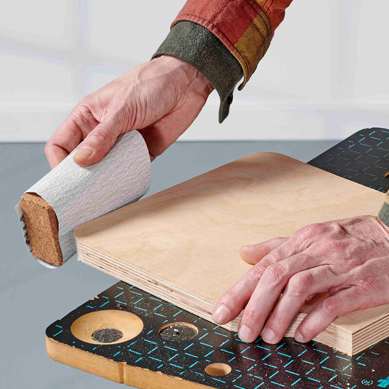 Mann schleift mit Schleifpapier die Kanten einer Multiplexplatte
