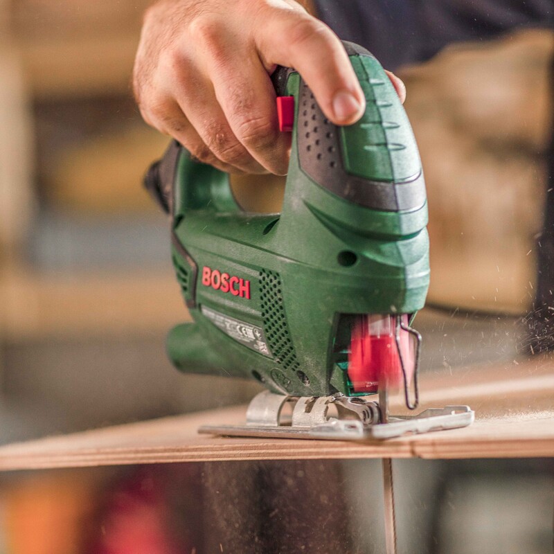 Eine handliche Stichsäge schneidet durch die Holzplatte