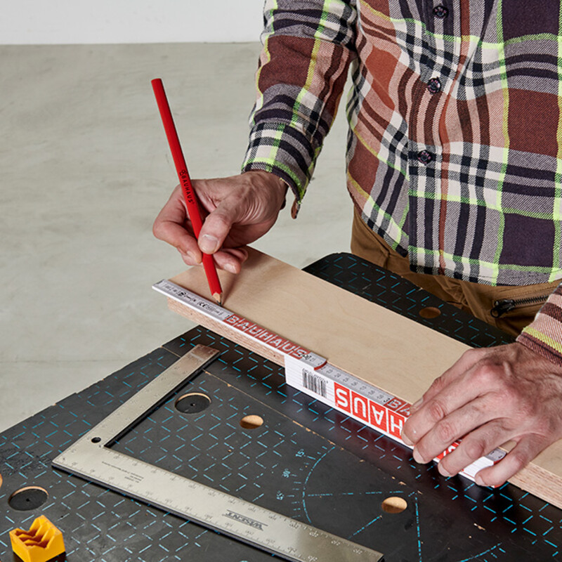 Mann im karierten Hemd zeichnet mit Bleistift auf Holz