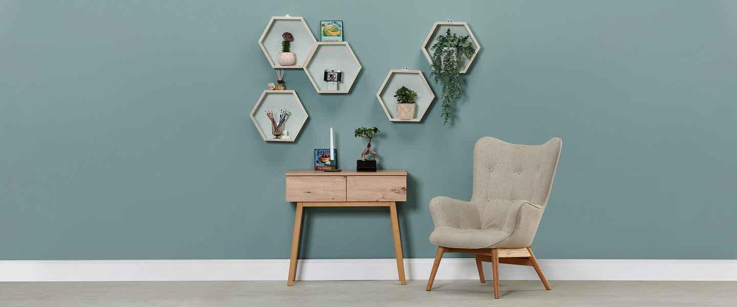 Blau gestrichene Wand mit einem Sessel, einer Konsole steht davor und 5 Wabenregal-Elemente hängen an der Wand