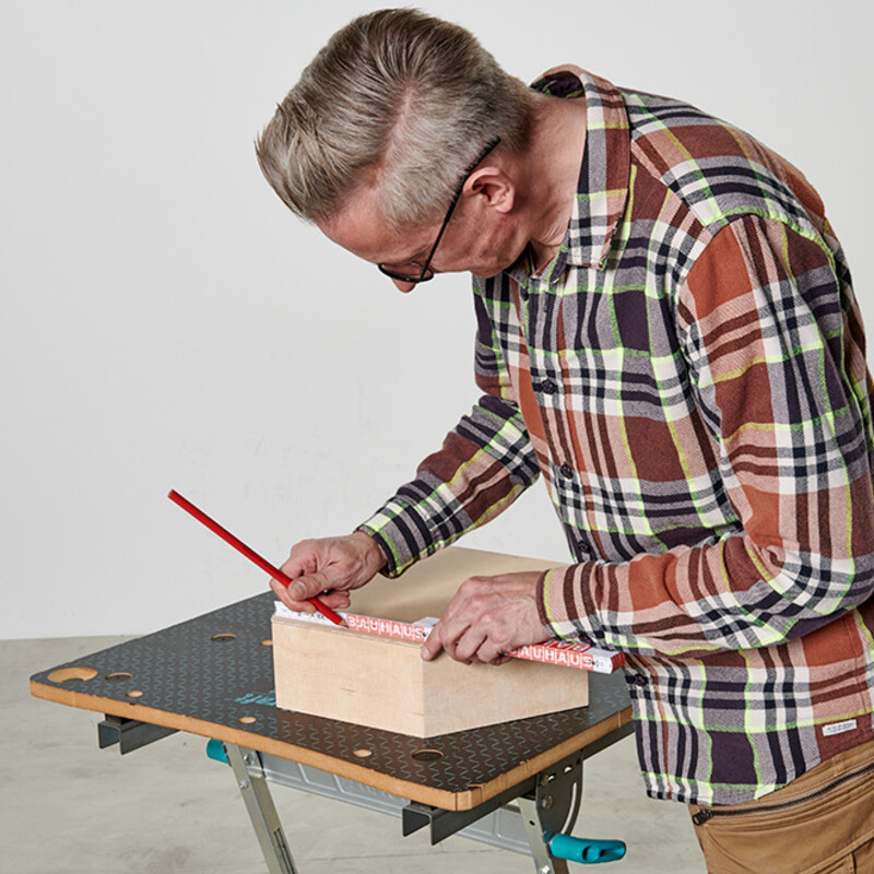 Mann zeichnet mit Bleistift auf einem Holzkorpus