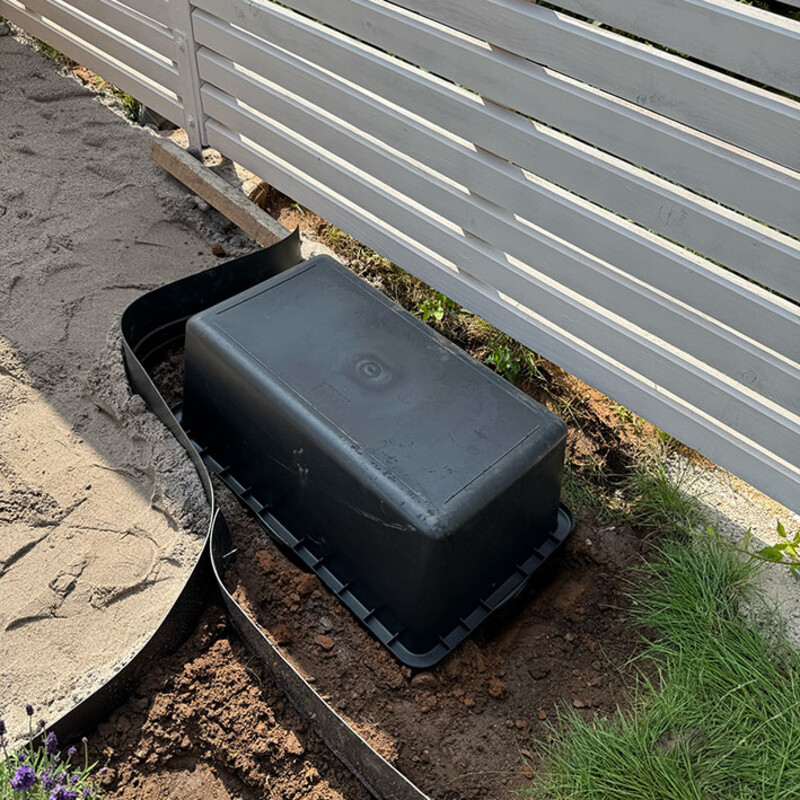 Umgedrehter schwarzer Mörtelkasten vor Gartenzaun