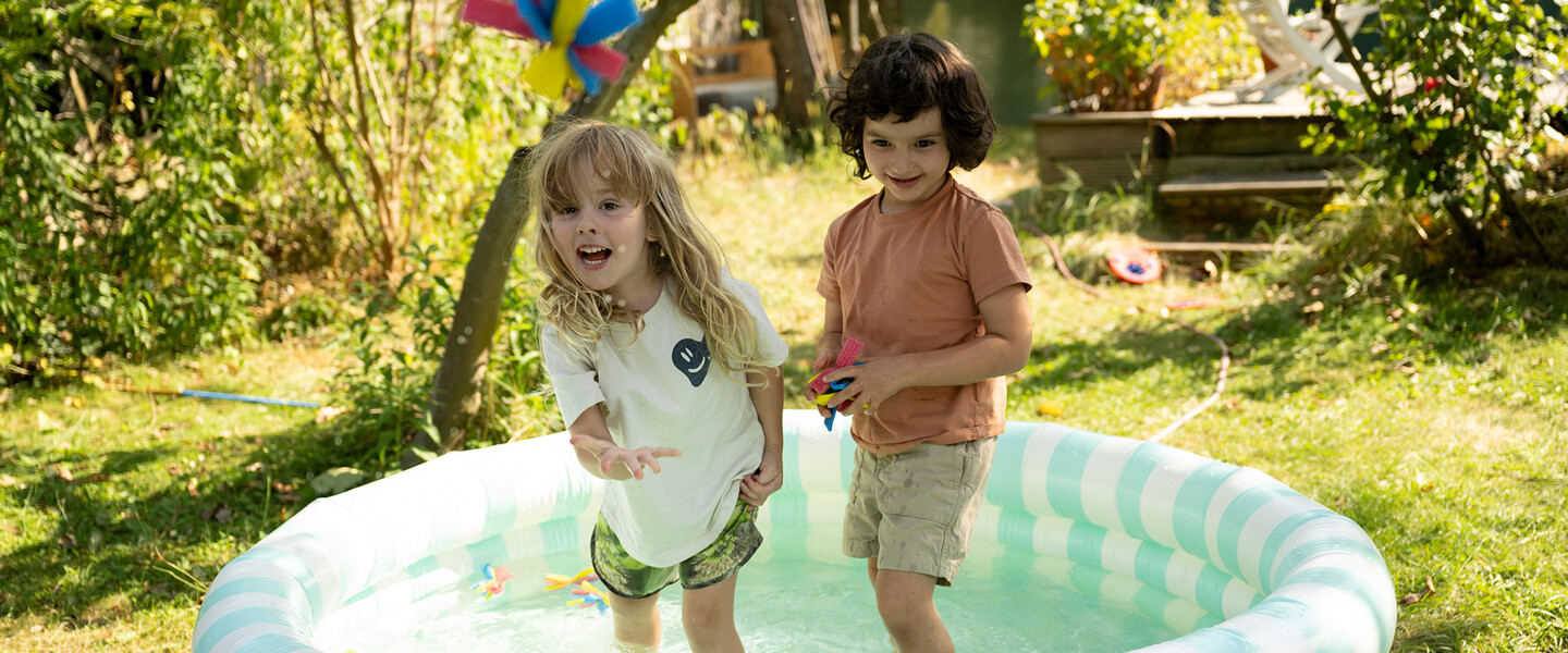 Zwei Kinder stehen in einem Planschbecken und spielen mit selbstgebastelten Wasserbomben