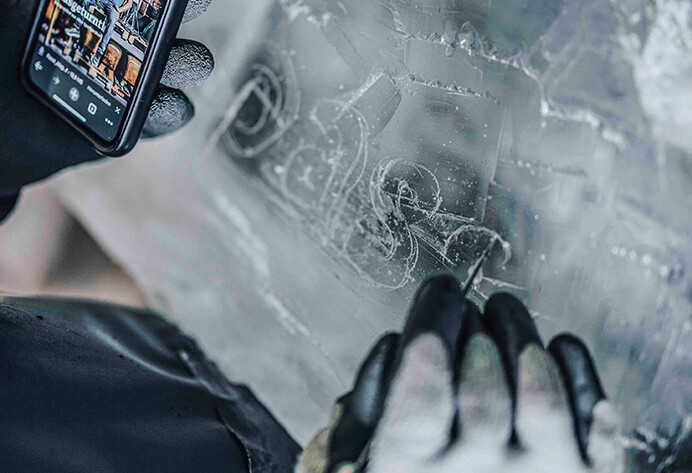 Mann schaut auf Handy und kratzt einen Schriftzug in eine Eisskulptur