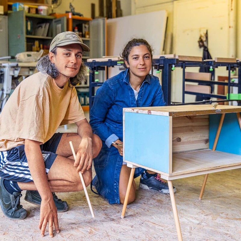 Mann und Frau sitzen in Werkstatt neben selbstgebautem Regal
