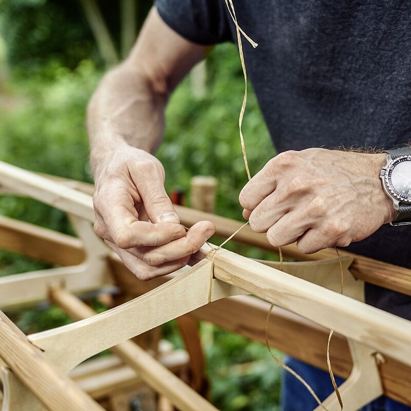 Mann bindet Faden um Holzgerippe eines selbstgebauten Kanus