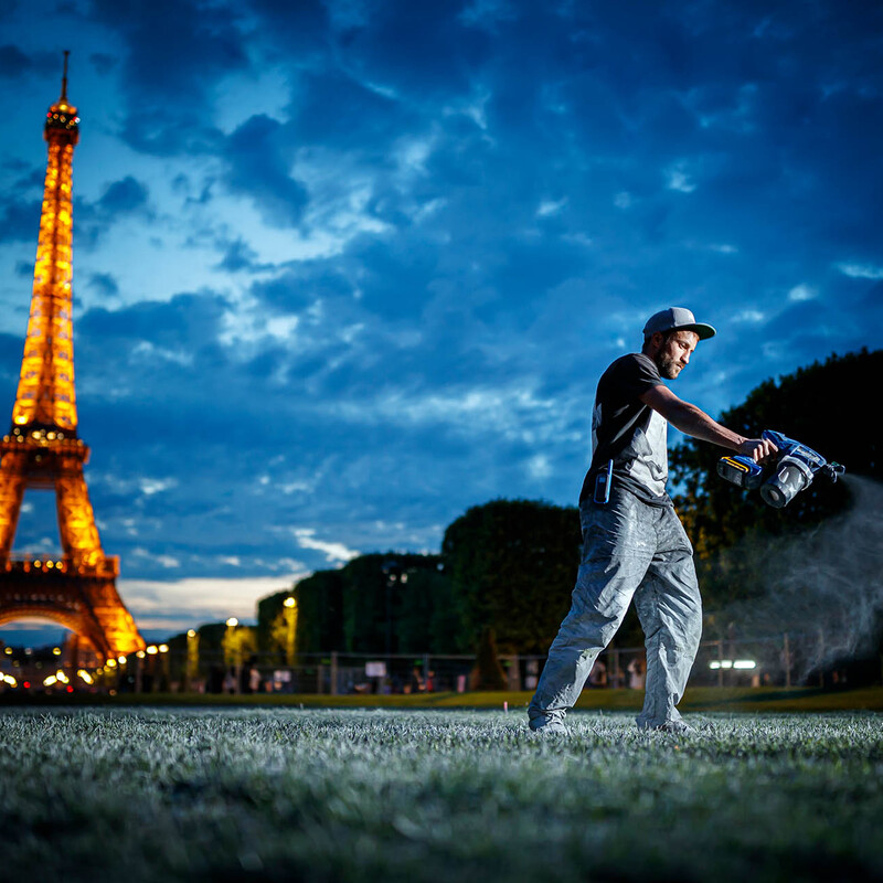 Mann mit Sprühgerät arbeitet auf der Wiese vor dem Eiffelturm in der Abenddämmerung