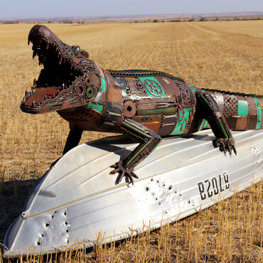 Metallskluptur eines Aligators auf einem umgedrehten Boot auf einem Feld