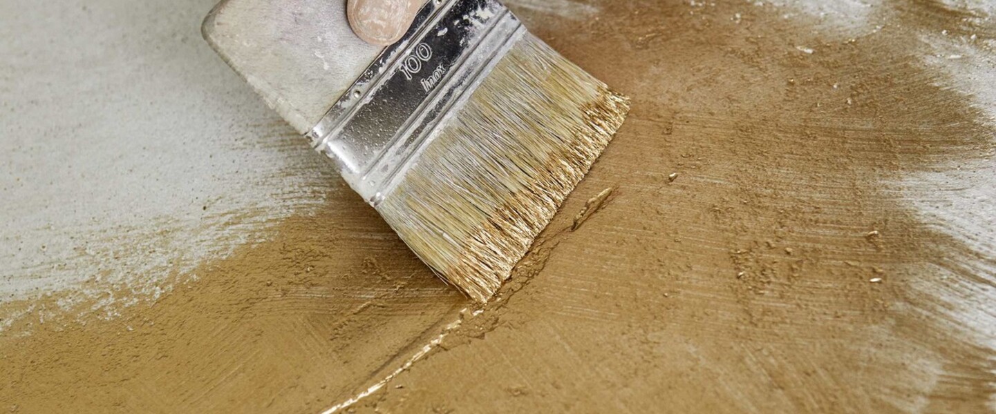 Hand mit breitem Pinsel streicht goldene Farbe auf eine Platte