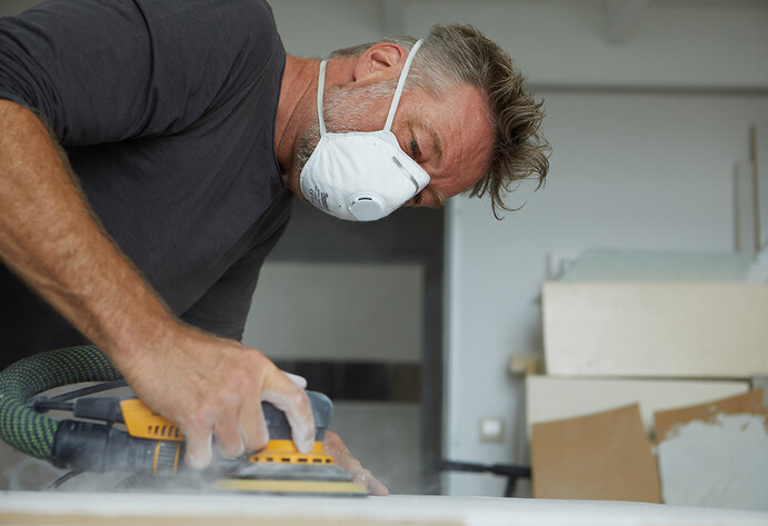 Mann mit Schutzmaske arbeitet mit Schleifgerät