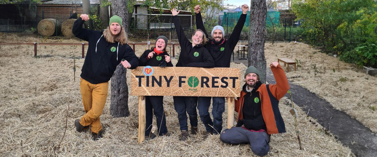 Das Team von MIYA Forest posiert für die Kamera hinter einem Holzschild