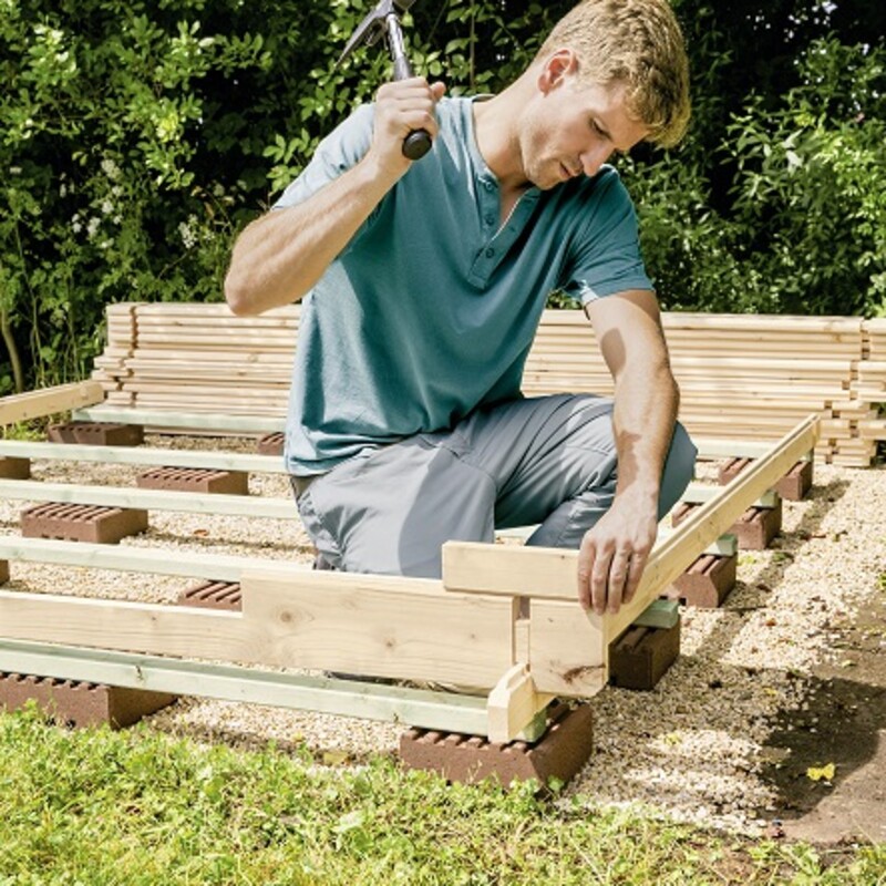 Mann schlägt Nägel in die Blockbohlen