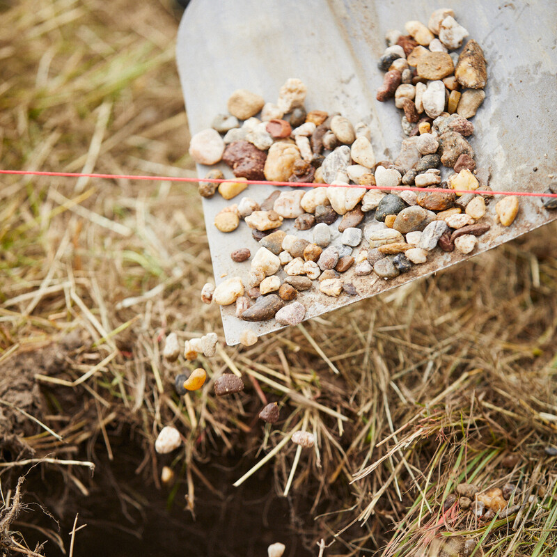 Maschendrahtzaun aufstellen: Drainagekies in Pfostenlöcher füllen