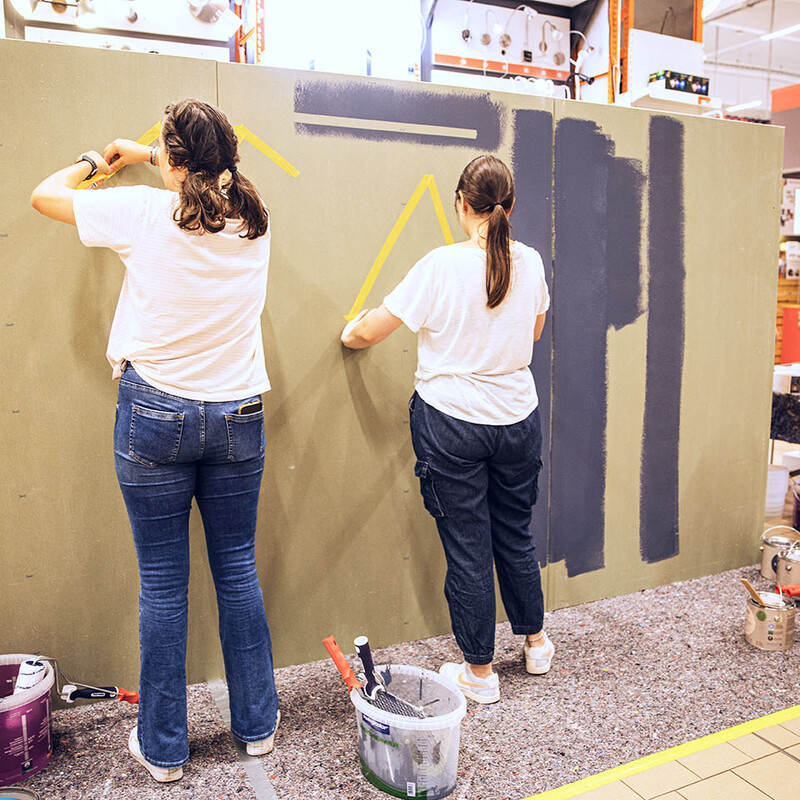 Zwei Frauen kleben Klebeband an eine Wand