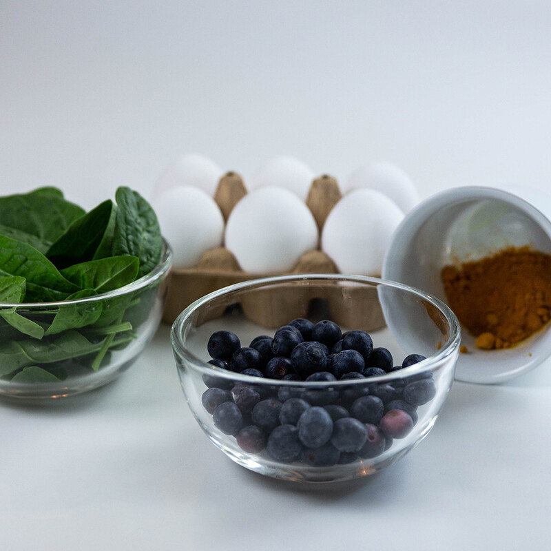 Spinat, Heidelbeeren und Kurkuma in Gefäßen vor Eiern