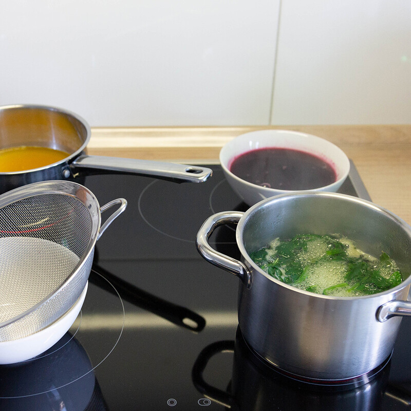 Spinat, Heidelbeeren und Kurkuma in verscheidenen Töpfen auf Herdplatten
