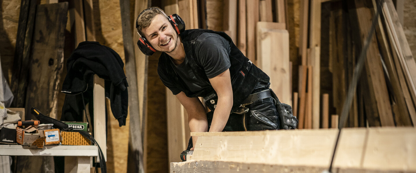 Zimmermann arbeitet mit Geh&ouml;rschutz an Holzbalken