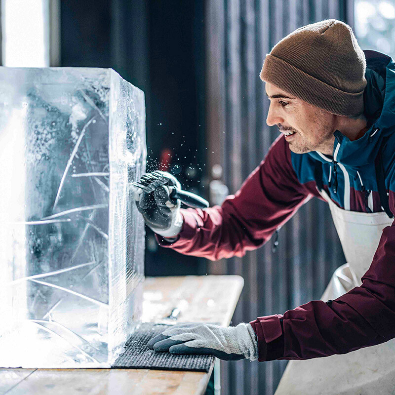 Mann mit Mütze kratzt mit Kratzer eine Linie in einen Eisblock