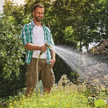 Mann bew&auml;ssert Plfanzen im Garten mit einem Gartenschlauch