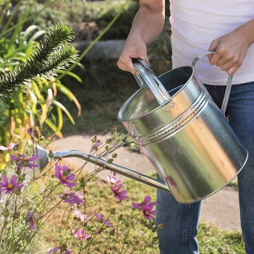 Eine Frau gie&szlig;t drau&szlig;en Blumen mit einer silbernen Gie&szlig;kann