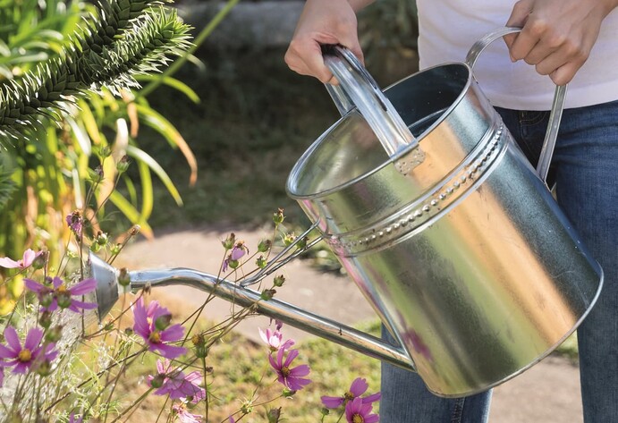 Eine Frau gie&szlig;t drau&szlig;en Blumen mit einer silbernen Gie&szlig;kann