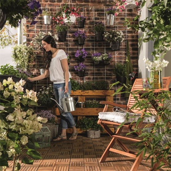 Eine Frau steht auf dem Balkon und gie&szlig;t ihre Pflanzen