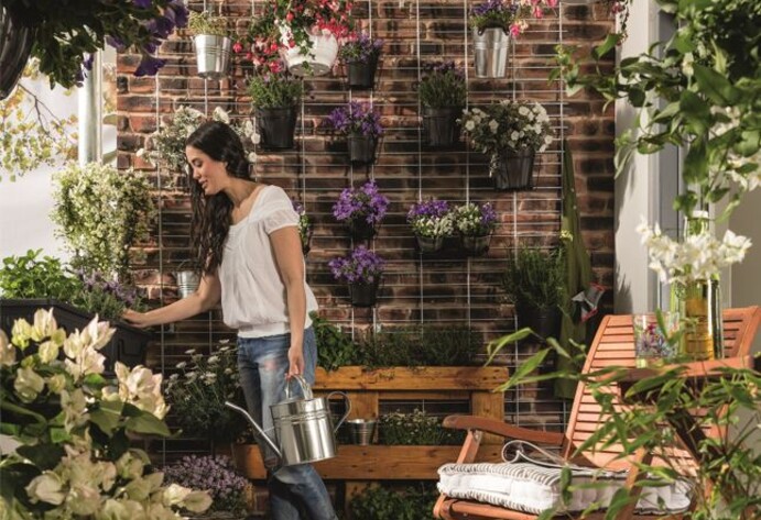 Eine Frau steht auf dem Balkon und gie&szlig;t ihre Pflanzen
