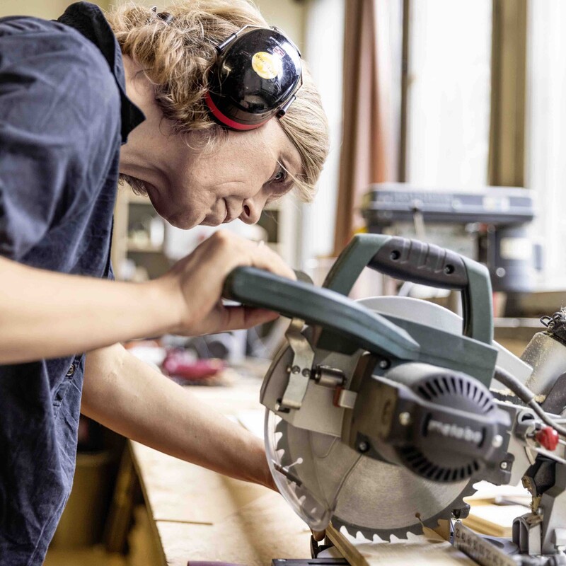 Frau in Werkstatt schneidet Holz mit Kapps&auml;ge