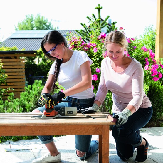 Zwei Frauen schleifen Holbank zusammen ab und halten diese fest