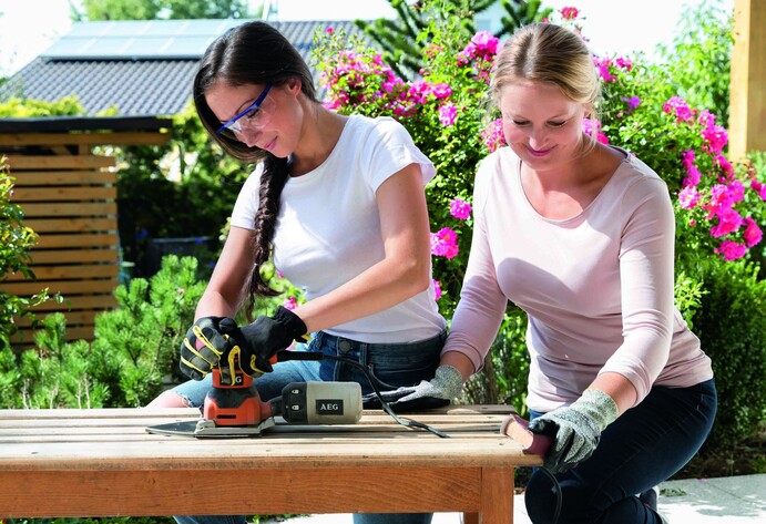 Zwei Frauen schleifen Holbank zusammen ab und halten diese fest