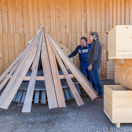 Zwei ältere Männer stehen neben einer spitzzulaufenden Holzkonstruktion