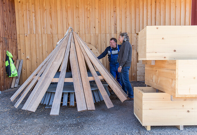 Zwei ältere Männer stehen neben einer spitzzulaufenden Holzkonstruktion