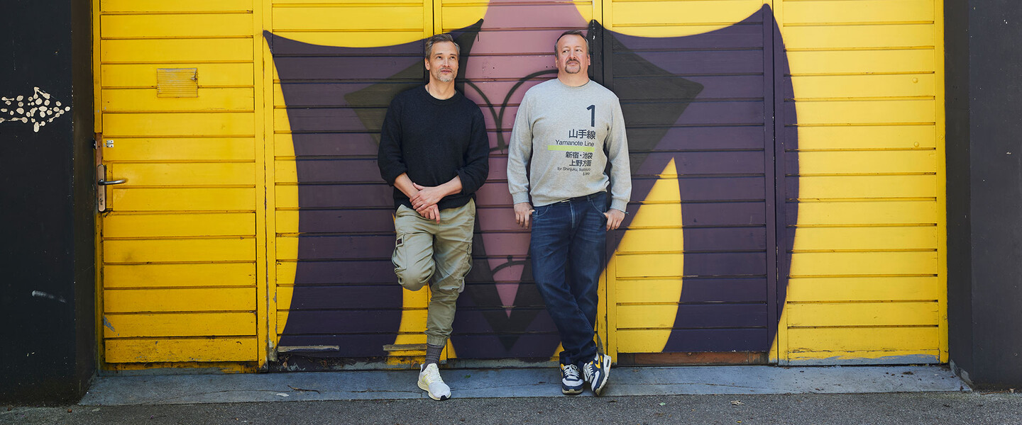 Zwei M&auml;nner stehen angelehnt vor einer Graffit-Wand