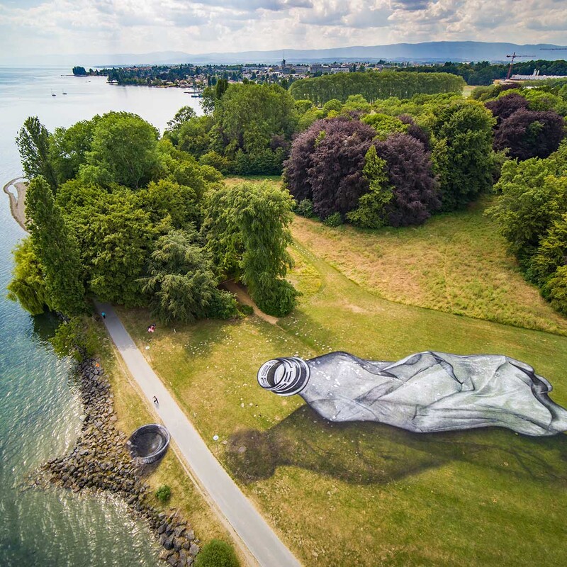 Gezeichnete PET-Flasche in Übergröße auf Wiese gemalt neben See