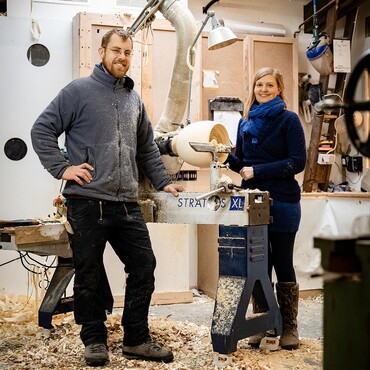 Ein Mann und eine Frau stehen in einer Werkstatt neben einer Drechselbank