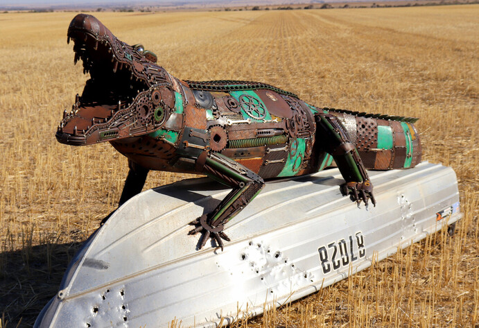 Metallskluptur eines Aligators auf einem umgedrehten Boot auf einem Feld