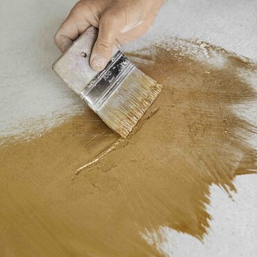 Hand mit breitem Pinsel streicht goldene Farbe auf eine Platte