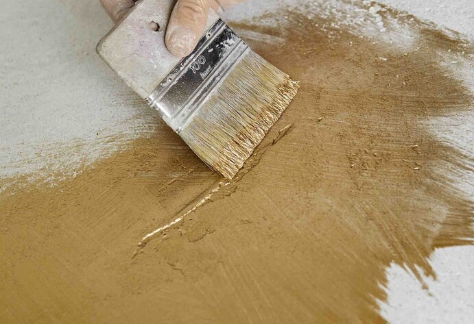 Hand mit breitem Pinsel streicht goldene Farbe auf eine Platte