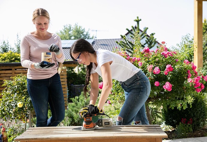 Zwei Frauen bearbeiten eine Holzbank im Außenbereich