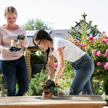 Zwei Frauen bearbeiten eine Holzbank im Außenbereich