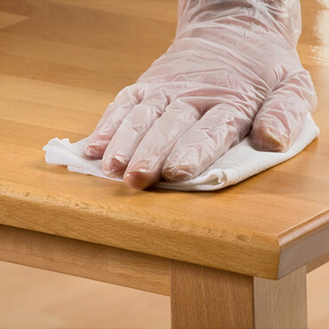 Hand mit Handschuh ölt Holztisch ein